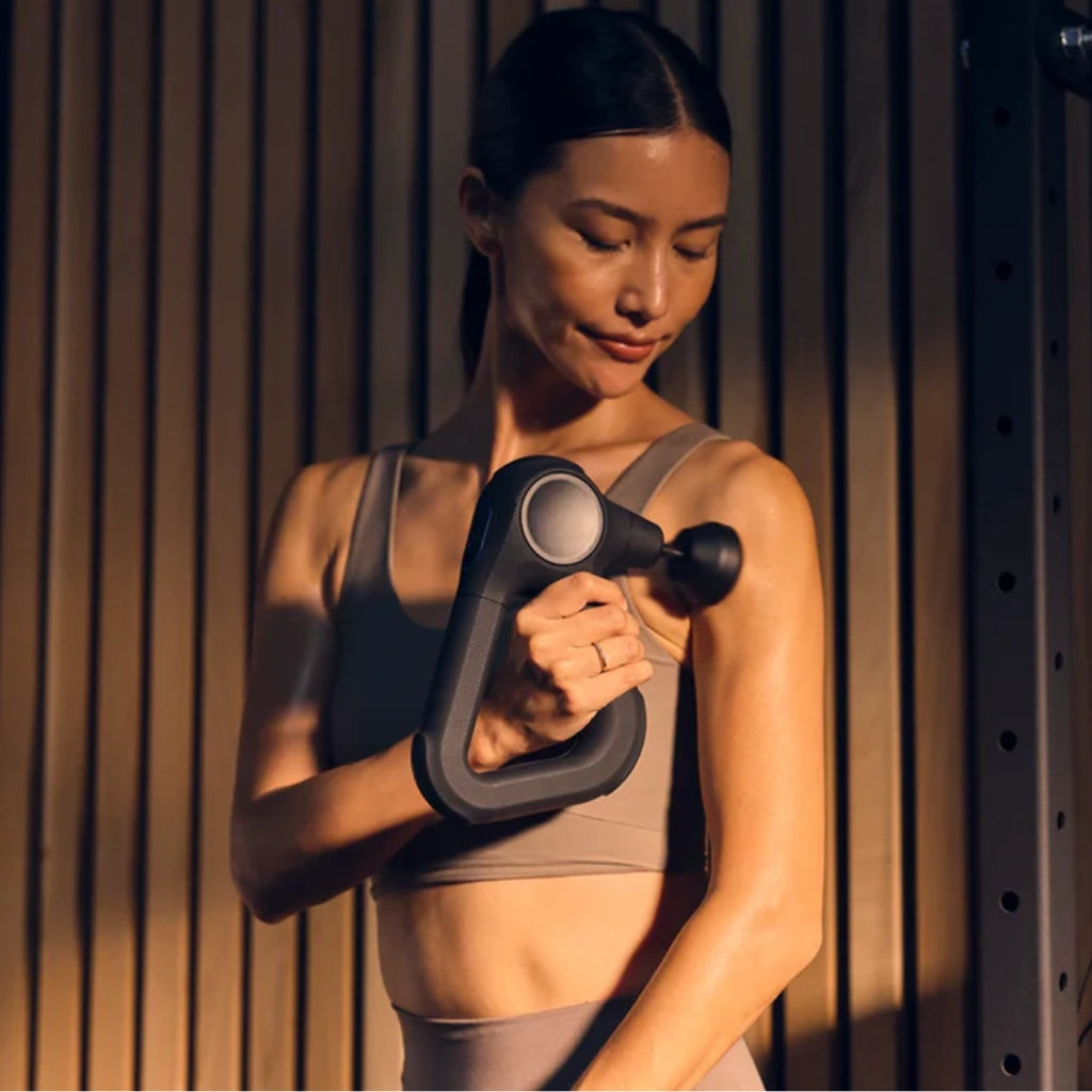 Woman using a massage gun / massagepistol with a wooden background